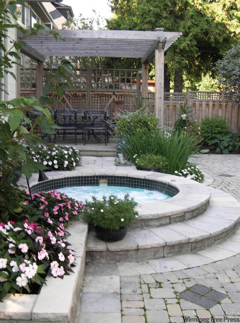 Rimmed with lush flower beds and intricate stonework, a swirling hot tub is the focal point of this private courtyard. A cedar pergola above the dining table provides shelter from the sun. 