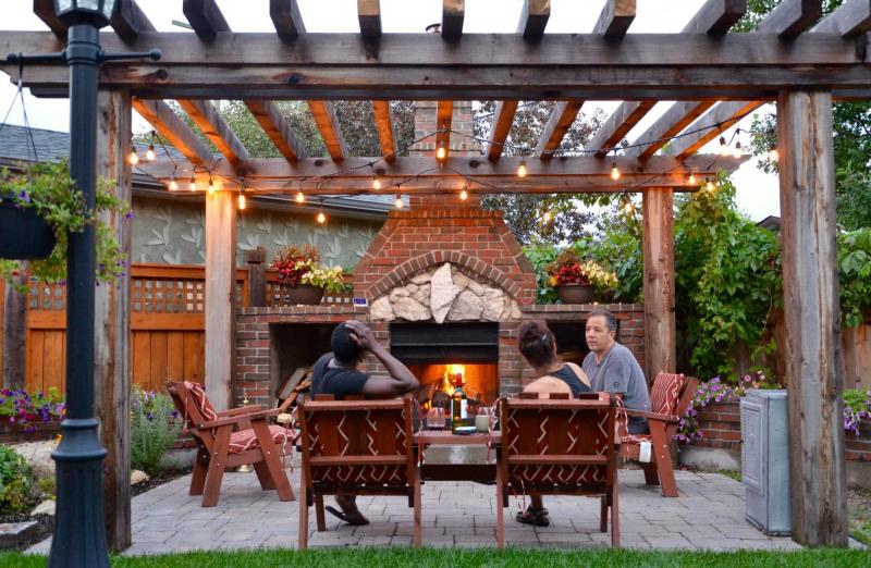 <p>Jessika Aiello</p><p>Mario and Silvia Aiello relax with a neighbour and a glass of wine in front of the brick fireplace that Mario built.</p>
