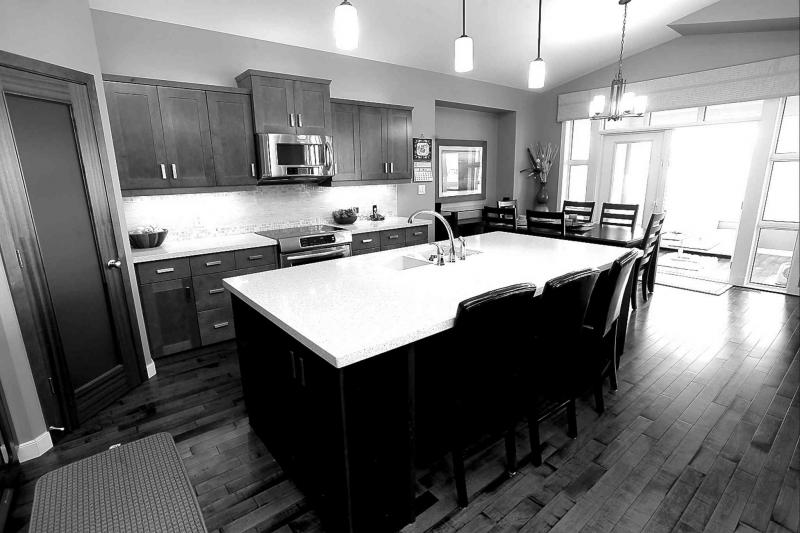 A chef's kitchen features a cherry-stained, nine-foot by four-foot island with a beige quartz countertop and seating for three.
