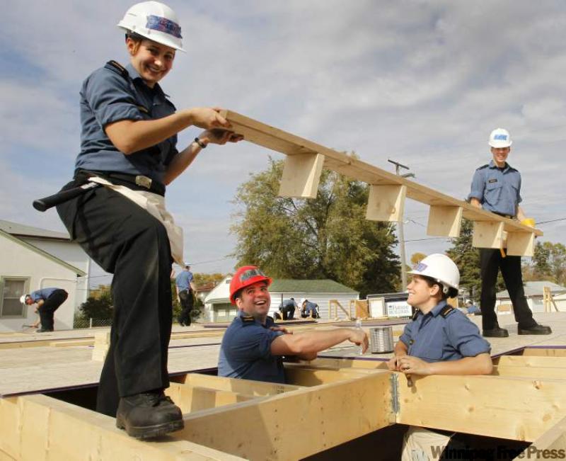 Caroline Brodeur and Nathan Broda lift a floor joist over Patrick Gray and Sarah Charbonneau who along with ten other officers and sailors of HMCS Winnipeg work on Habitat for Humanity homes earlier this year.  A record 23 Habitat homes were built this year.