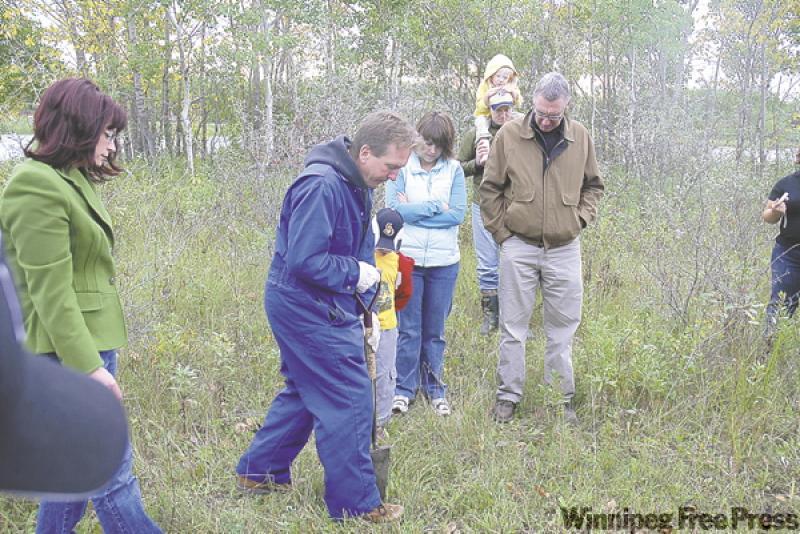 Ken Fosty of the Manitoba Forestry Association, with volunteers, demonstrates how to plant a seedling.