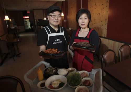 MIKE.DEAL@FREEPRESS.MB.CA 110420 - Wednesday, April 20, 2011 - The Nou Eul Tor Korean Restaurant 726 Sargeant Ave (l-r) Jay Yoo and his wife Ju Hee Kim holding Gochujan Samgyopsal and Pulgogi hot plates with a cart that has a bowl of Gamjatang and Bibimbap as well as various side dishes which are customary. MIKE DEAL / WINNIPEG FREE PRESS