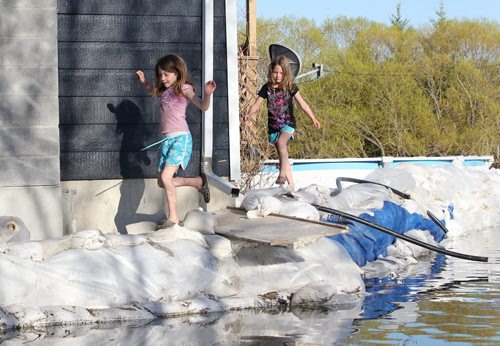 Brandon Sun 15052011 Sisters Emmalee and Sadies Poczik play along the sandbag dike protecting their grandparents home on Grand Valley Rd. as the descending sun reflects off of the flood waters on Sunday evening. (Tim Smith/Brandon Sun)
