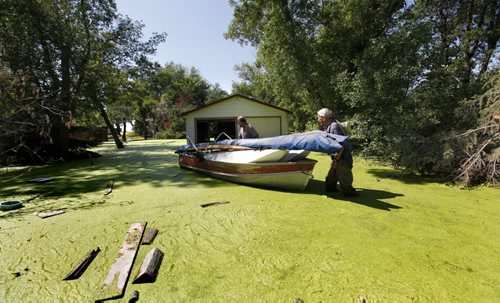 Albert Jacobs (hat) pushes his boat with help from his son Dave through stagnant water covered in green algae as they move personal belongings from Albert and his wife Elsie's home at 49 Twin Lakes Beach Rd. at Twin Beaches.  The couple in their 80's have been living in their home at the lake for over 25 years are now forced to leave it and rent a apartment in the city due to high water on Lake Manitoba seeping into their crawl space. Photo's of Twin Lakes Beaches. Saturday Special, Follow-up on Manitoba 2011 Flood by Melissa Martin. July 27, 2011 (RUTH BONNEVILLE / WINNIPEG FREE PRESS)