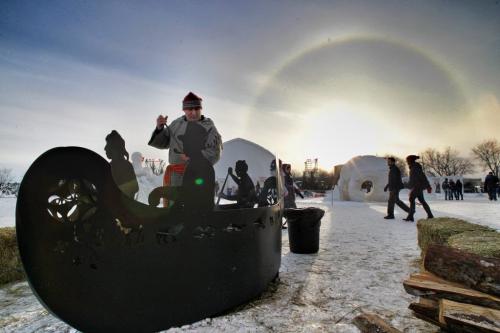 Kevin Cleveland tends the fire in an ornate fire pit shaped like a canoe on the grounds of the Festival du Voyageur while the sun sets with a sundog Saturday evening.  120225 Mike Deal / Winnipeg Free Press