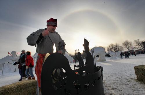 Kevin Cleveland tends the fire in an ornate fire pit shaped like a canoe on the grounds of the Festival du Voyageur while the sun sets with a sundog Saturday evening.  120225 Mike Deal / Winnipeg Free Press