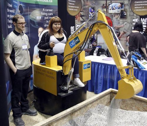 Tamara Young-Skye a student at Ka Ni Kanichihk Inc. tries out the excavator simulator beside Billy Elias at the Operating Engineers Training Institute of Manitoba Inc. booth on the show floor of the Rotary Career Symposium Wednesday at the Winnipeg Convention Centre. Organizers of the two day symposium are expecting approximately 12,000 Manitoba students and 3000 members of the general public who will get  an opportunity to gain valuable information about various education and employment options.       (WAYNE GLOWACKI/WINNIPEG FREE PRESS) Winnipeg Free Press  April 4  2012