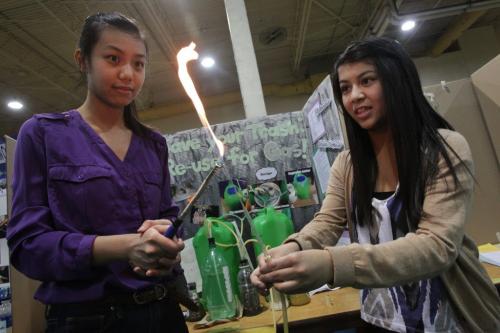 Judging takes place at the Manitoba Schools' Science Symposium in the Max Bell Field-house at the University of Manitoba.   Lisa Huang (left) , 15, and Megan Esguerra, 15, from Sisler High School designed a small-scale biogas digester based on a pressurized fixed dome design. Their project is titled "Save your Trash: Re-use for Gas!" To show that a gas is being produced Lisa holds a small flame to a valve that can release gas from the storage tank.  120428 April 28, 2012 Mike Deal / Winnipeg Free Press