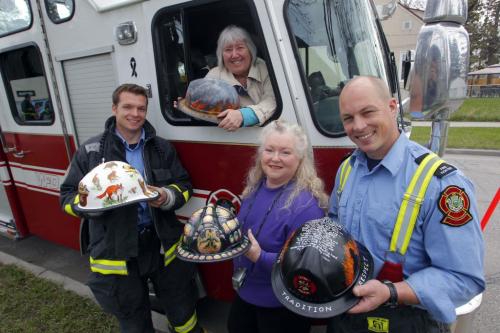 Artists Suzanne Barrow (up in truck), and Carleigh Duncan-Doyle are flanked by firefighters (left) Keith Scott and Ryan Whitely(right). (from Press release) Get a sneak preview of what happens when local artists put their talent to work and turn well-used firefighter helmets into works of art for the Firefighters Burn Fund. Weeks ago, artists adopted helmets that have been taken out of service after being used by firefighters on the job.  The artists return them today transformed into works of art.  The helmets are unpacked and put on display from 10:30 a.m. to noon today in preparation for the launch of the Burn Fund Silent Auction Fundraiser starting this evening.  Media are invited to get a sneak peak at what happens when firefighters and artists get together for a good cause. Photo taken at 180 Poplar Ave. at Brazier St., Elmwood East Kildonan Active Living Centre, Wpg. May 4, 2012  BORIS MINKEVICH / WINNIPEG FREE PRESS