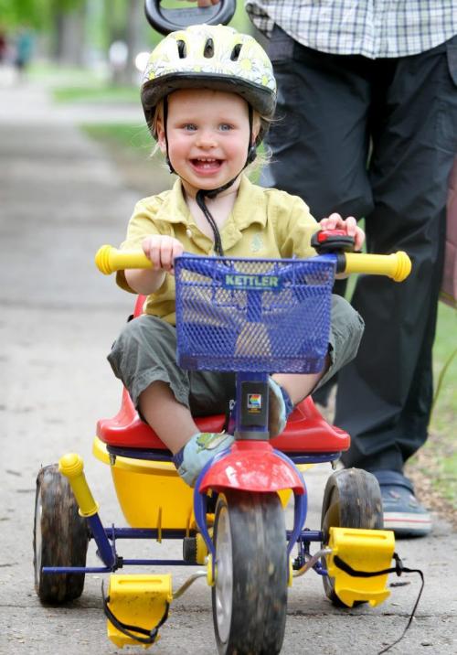 Eighteen month old Jamie Main Prize laughs as he watches his older sister play in frotn of him while going for a ride along on his trike in their River Heights neighborhood Wednesday afternoon with dad.  See story on helmet law. May 23  2012 (Ruth Bonneville/Winnipeg Free Press) bike helmet kid