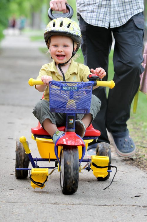 Eighteen month old Jamie Main Prize laughs as he watches his older sister play in frotn of him while going for a ride along on his trike in their River Heights neighborhood Wednesday afternoon with dad.  See story on helmet law. May 23  2012 (Ruth Bonneville/Winnipeg Free Press)  bike helmet kid