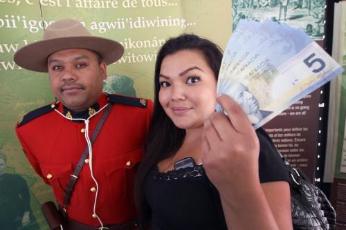 Stephanie Woodhouse from the Pinaymootang First Nation stands with RCMP Cpl. Gabriel Simard as she holds a handful of $5.00 bills she collected on behalf of herself and children. The annual treaty payment, administered by Indian and Northern Affairs Canada and Parks Canada were handed out today at the Forks in Winnipeg. The yearly $5 payment is part of seven numbered treaties signed on behalf of First Nations communities across the province in the 1800s and early 1900s.  annuity payments will be available at the Forks from June 12-28, 2012- June 12, 2012   (JOE BRYKSA / WINNIPEG FREE PRESS)