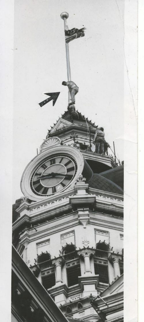 Winnipeg Free Press Archives Winnipeg Old City Hall (7) July 16, 1957 Maybe B. J. "Jim" Morrissett hasn't heard about the dangers of the city hall tower. For Mere Mr. Morrissett, - and a steeplejack for Fort Rouge Decorating and Sandblasting, doesn't seem to be worried as he scales to the top of the flagpole, 50 feet above the controversial tower. Last week the flagpole rope snapped in a high wind and the flag draped over one of the faces of the tower clock. Jim was called in at 8 a.m.. Tuesday to pass a new rope through the pulley at the top of the pole. This is the third time he has been up in the last, several years and he says  that "it's getting a little shakier each time." fparchive