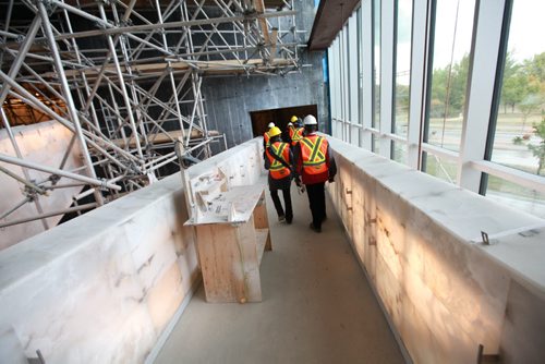 Members  of the media walk down wide ramps finished in alabaster and illuminated from within its shell as they make their way to the main entrance Wednesday after touring the structure. Earlier building crews working on the Canadian Museum of Human Righs hoisted  the final piece of glass up to the chimney area of the Tower of Hope  which is 328 feet high on Wednesday morning. See Story Sept 20,  2012 (Ruth Bonneville/Winnipeg Free Press) CMHR