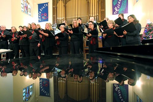 Brandon Sun 15122012 The Bel Canto adult choir is reflected in the top of a piano as they perform traditional Christmas songs during the 32nd Annual Christmas with the Conservatory Chorale concert at First Presbyterian Church in Brandon on Sunday. The concert included performances by a variety of the Conservatory choirs.  (Tim Smith/Brandon Sun)