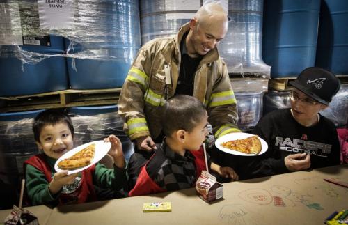 (l-r) Cameron Cutlip, 7, Tyrell Gottchock, 7, and his auntie April Flett from Dufferin School are served some pizza by firefighter S. Jones while they wait for Santa to arrive. Around 150 kids from three Winnipeg School Division elementary schools, Strathcona, Mulvey and Dufferin, got to have lunch in the Winnipeg James Armstrong Richardson International Aiport's firehall where Santa just happened to be testing out the STARS helicopter. Fred Penner was on hand to perform some music too. 121217 - Monday, December 17, 2012 -  (MIKE DEAL / WINNIPEG FREE PRESS)