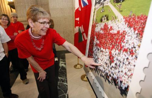 in pic  Living Flag volunteer Carolynn MacKenzie  finds herself in an enlargeded version of the stamp after the newser. Canada Post has released a new stamp depicting Winnipeg's  Canada Day Living Flag from 2012  , 3000 Manitobans  volunteered wearing red and white t-shirts to make flag on the Manitoba Legislative grounds .Bruce Owen story  KEN GIGLIOTTI / JAN 14 2013 / WINNIPEG FREE PRESS. Original photo of the living flag taken for Canada Post by Dan Harper.