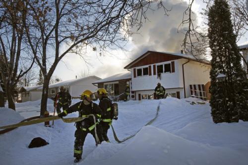 Fire heavily damaged a home at 54 Merrill Cres. near Antrim , there were no injuries ,the fire apparently started in upper level rear of the split level house around 12:45 pm - fire fighters rush to get extra hose to the homes front entrance and second floor  as fire raged at rear . KEN GIGLIOTTI / JAN. 25 2013 / WINNIPEG FREE PRESS