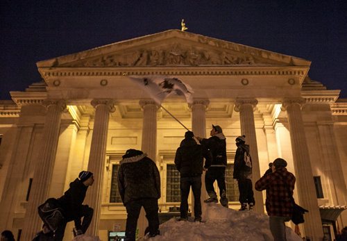 Youth stand atop a snow bank waving a flag in front of the Manitoba Legislature during an Idle No More rally Monday evening. Several hundred people attended the rally, where Buffy Sainte-Marie spoke and sang before a giant round dance surrounded part of the Legislature. (Melissa Tait / Winnipeg Free Press)