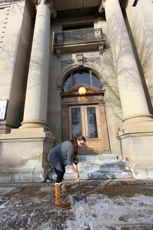 Brandon Sun 13022013 Becky Farguson with the Brandon Chamber of Commerce chips away ice in front of the Rosser Ave. building on a warm Wednesday afternoon. (Tim Smith/Brandon Sun)