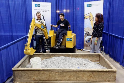 Brandon Sun 05032013 Fleming High School student Annie Cloud operates a scaled down digger as Billy Elias with Operating Engineers Training Institute of Manitoba and friend Leigha Cloud look on during the 28th Annual Brandon Career Symposium at the Keystone Centre on Tuesday. (Tim Smith/Brandon Sun)