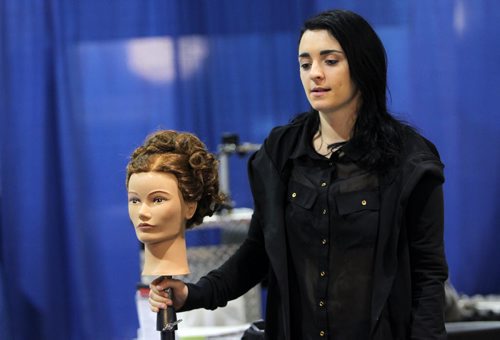 Brandon Sun 05032013 Caitlin Bousfield, a hairstyling student with Winnipeg Technical College, holds a mannequin head while greeting visitors to the college's booth at the 28th Annual Brandon Career Symposium at the Keystone Centre on Tuesday. (Tim Smith/Brandon Sun)