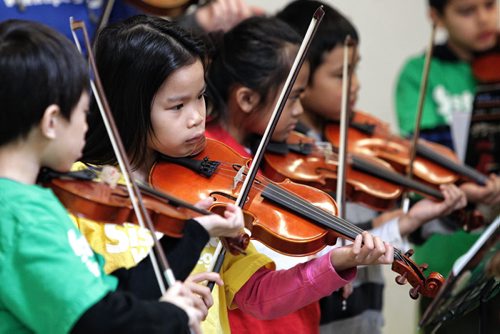 Elwick school student, AJ Rosaldo (second from left), 8, plays her violin along with about 30 other grade 2 and 3 students who are part of the Sistema after school program. They performed for Winnipeg Harvest volunteers Monday afternoon thanking the organization for providing food for their after school program.  130318 March 18, 2013 Mike Deal / Winnipeg Free Press