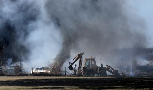A man walks alongside a front end loader moving through a field of burning derelict vehicles along Oak Hammock Road in St Andrews Monday. Fire Departmets from St Andrews were joined by West St Paul fighting the blaze. See story. May 13, 2013 - (Phil Hossack / Winnipeg Free Press)