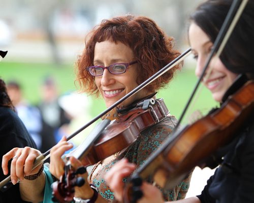 Miriam Neuman (left, red hair) fiddles with local fellow fiddlers under the canopy at Coronation Park Saturday afternoon for the 1st annual World Fiddle Day.  (Emilie Chartier, black hair to her left) Standup photo  May 18, 2013 Ruth Bonneville Winnipeg Free Press