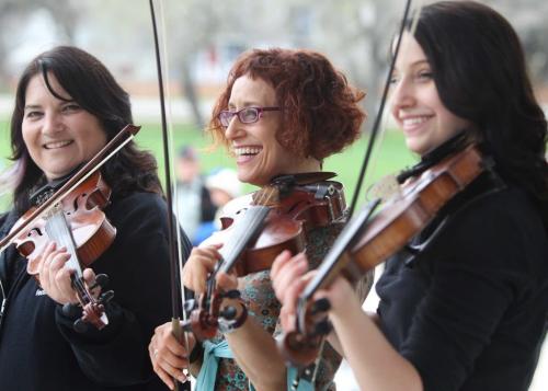 Miriam Neuman (left, red hair) fiddles with local fellow fiddlers under the canopy at Coronation Park Saturday afternoon for the 1st annual World Fiddle Day.  (Emilie Chartier, black hair to her left and Patti Lamoureux her right). Standup photo  May 18, 2013 Ruth Bonneville Winnipeg Free Press