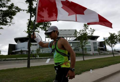 A full marathoner carries a Canadian Flag past Investors Group Field along Chancellor Matheson Drive on the way to the finish line at the University of Manitoba during the 35th Annual Manitoba Marathon, Sunday, June 16, 2013. (TREVOR HAGAN/WINNIPEG FREE PRESS)