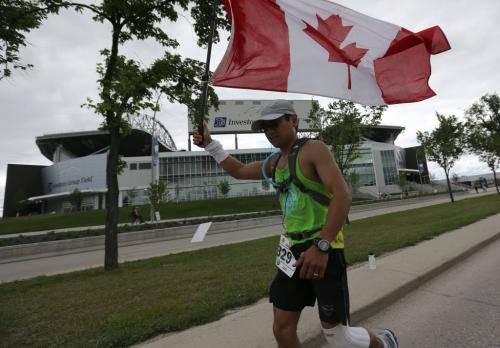 A full marathoner carries a Canadian Flag past Investors Group Field along Chancellor Matheson Drive on the way to the finish line at the University of Manitoba during the 35th Annual Manitoba Marathon, Sunday, June 16, 2013. (TREVOR HAGAN/WINNIPEG FREE PRESS)