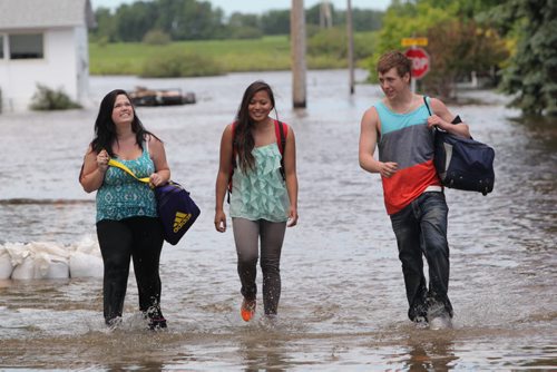 Brandon Sun 26062013 Daveena Zorn, Natasha Morrison and Garrett Adcock walk along a flooded street in the community of Reston after Adcock's vehicle stalled on a flooded road outside of town on Wednesday. The trio were headed home from Zorn's grad which was the previous day and had to walk to Reston when their vehicle became flooded. (Tim Smith/Brandon Sun)