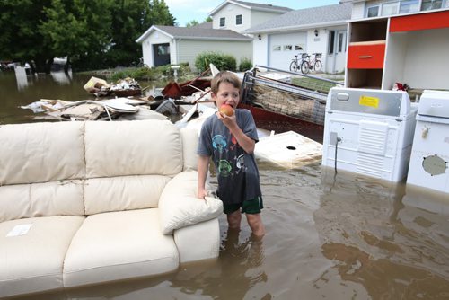 Brandon Sun 26062013 Six-year-old Aiden Sanderson eats an apple while walking through the flood water on 2nd Street in the community of Reston on Wednesday. Several families whose homes were flooded over the weekend were in the midst of cleaning up when Tuesday evenings storm caused flooding again.  (Tim Smith/Brandon Sun)