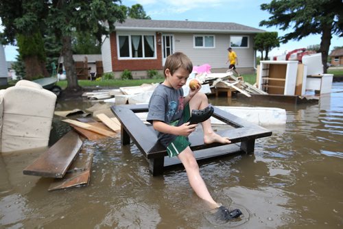 Brandon Sun 26062013 Six-year-old Aiden Sanderson eats an apple while exploring the flood water on 2nd Street in the community of Reston on Wednesday. Several families whose homes were flooded over the weekend were in the midst of cleaning up when Tuesday evenings storm caused flooding again.  (Tim Smith/Brandon Sun)