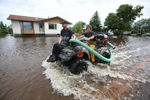 Brandon Sun 26062013 Young men drive a quad along a flooded street in the community of Reston while helping in the flood relief efforts on Wednesday. (Tim Smith/Brandon Sun)