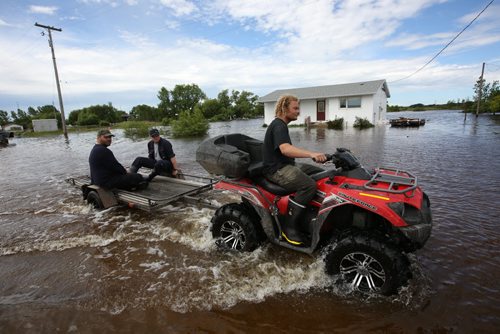Brandon Sun 26062013 Men drive a quad along a flooded street in the community of Reston while helping in the flood relief efforts on Wednesday. (Tim Smith/Brandon Sun)