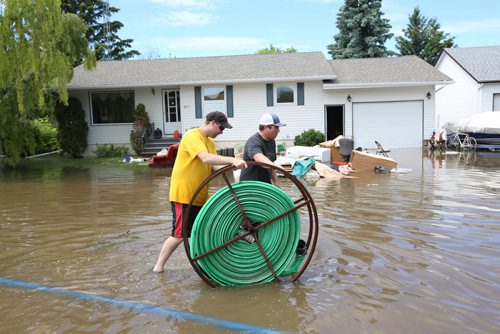 Brandon Sun 26062013 Vince Moore and Chris Flannery help set up pumps to pump water off 2nd Street in the community of Reston on Wednesday. Their homes were high and dry so they volunteered to help those who weren't so fortunate.  (Tim Smith/Brandon Sun)