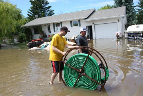 Brandon Sun 26062013 Vince Moore and Chris Flannery help set up pumps to pump water off 2nd Street in the community of Reston on Wednesday. Their homes were high and dry so they volunteered to help those who weren't so fortunate.  (Tim Smith/Brandon Sun)