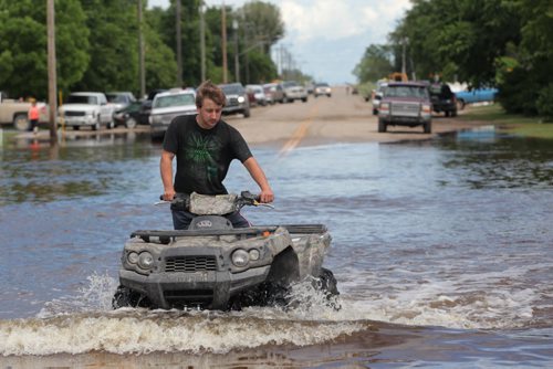 Brandon Sun 26062013 A young man drives a quad along a flooded street in the community of Reston while helping in the flood relief efforts on Wednesday. (Tim Smith/Brandon Sun)