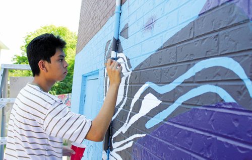 Canstar Community News  July 4, 2013 -- Christian Mariano, 18, colours in the fine details of a totem pole as part of a mural going up on the side of 7-Eleven at Mountain Avenue and McPhillips Street on July 4. The mural, sponsored by Take Pride Winnipeg, involved 25 students from the Wayfinders program in the Seven Oaks School Division. (MATT PREPROST/CANSTAR NEWS)