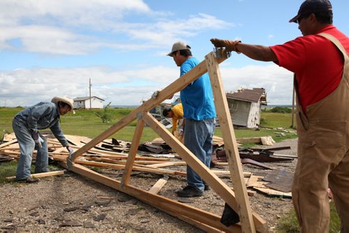 Brandon Sun 22072013 Volunteers Bill Maza, Dryden Wanbdiska, Colin Bunn and Rollie Bunn clean up the destroyed roof of a home at Sioux Valley Dakota Nation on Monday after homes were damaged by a tornado last Thursday. (Tim Smith/Brandon Sun)