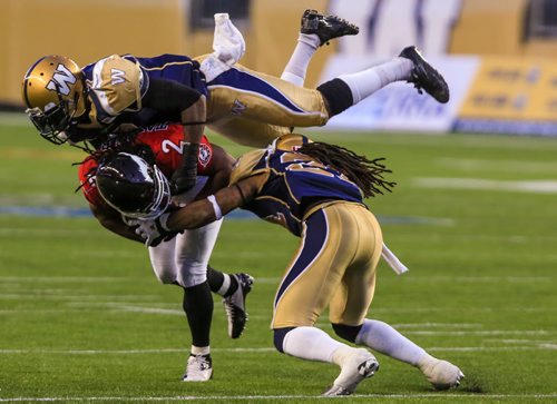 Bombers' defensive back Demond Washington flies over Stampeders' receiver Larry Taylor as Winnipeg's Alex Suber tries to strip the ball in the third quarter at Investors Group Field Friday night.  130726 - Friday, July 26, 2013 - (Melissa Tait / Winnipeg Free Press)
