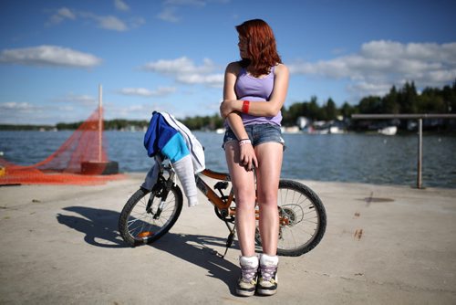 Brandon Sun 27072013 Lindsay Anderson of Brandon sits against a bike on the pier at Sandy Lake while watching friends fish on Saturday evening. (Tim Smith/Brandon Sun)