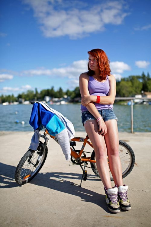 Brandon Sun 27072013 Lindsay Anderson of Brandon sits against a bike on the pier at Sandy Lake while watching friends fish on Saturday evening. (Tim Smith/Brandon Sun)