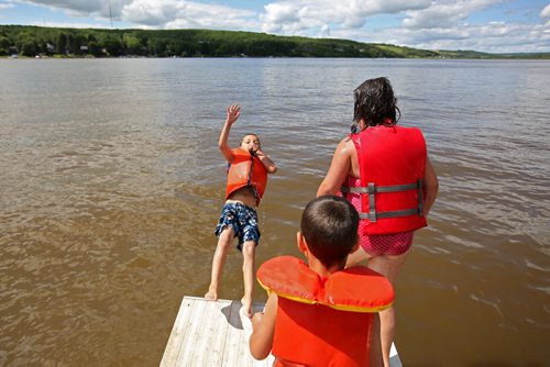 Brandon Sun 27072013 Siblings Keaston, Logan and Kadence Conley take turns leaping off the dock at the beach in the Minnedosa Beach Campground on Saturday. (Tim Smith/Brandon Sun)