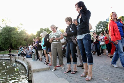 Jillian Hill a mother of two (right), looks out at the flowers in the Assiniboine River and wipes a tear during the candlelight vigil in memory of Lisa Gibson and her two children, two-year-old Anna and three-month-old Nicholas at The Forks Thursday evening. 130801 - August 01, 2013 Mike Deal / Winnipeg Free Press