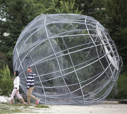 A couple walks past a gigantic spherical structure resting in the corner of a parking lot near Shaw Park on Friday afternoon. Friday, August 9, 2013. (JESSICA BURTNICK/WINNIPEG FREE PRESS)
A couple walks past a gigantic spherical structure in the corner of a vacant parking lot near The Forks Market Friday afternoon. The structure appears to be the skeleton of The Sunspot, a warming hut hung from the rail bridge over the frozen river trail in 2010 to provide skaters with shelter from wind and cold.