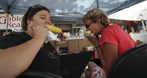 Allison Delaurier (left) and Jannine Alderson sneak a bite to eat behind their wall of Epicure spices up for purchase at the Festical. Established in 1967, the Morden Corn and Apple Festival is the town's chief attraction, and is always held in the fourth week of August. Friday, August 23, 2013. (JESSICA BURTNICK/WINNIPEG FREE PRESS)