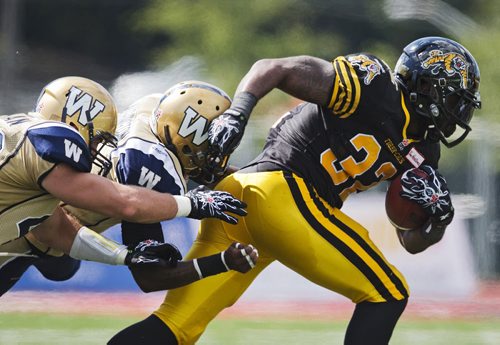 Hamilton Tiger-Cats C.J. Gable breaks the tackle of  Winnipeg Blue Bombers Demond Washington (C) and Rene Stephen (L) during the second half of their CFL football game in Guelph, August 24, 2013.    REUTERS/Mark Blinch (CANADA - Tags: SPORT FOOTBALL TPX IMAGES OF THE DAY) - RTX12VFI